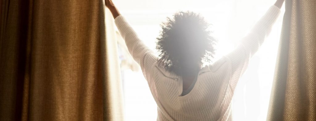 woman opening curtains to a new day